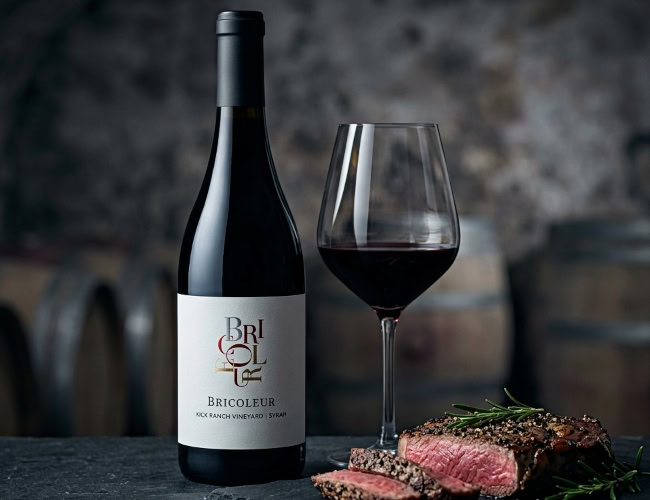 2022 Bricoleur Vineyards Kick Ranch Syrah — Fountaingrove District, Sonoma County 2022 Bricoleur Vineyards Kick Ranch Syrah bottle and wine glass paired with a pepper-crusted ribeye steak